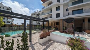 A modern residential building with a swimming pool, outdoor seating, and a pergola. - Aster Apartments (Villajoyosa)