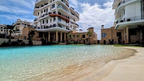 A modern apartment building with a swimming pool and a sandy beach area. - Aster Apartments (Villajoyosa)
