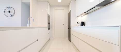 A modern kitchen with white cabinetry, a stainless steel refrigerator, a coffee maker, and a wall clock.
