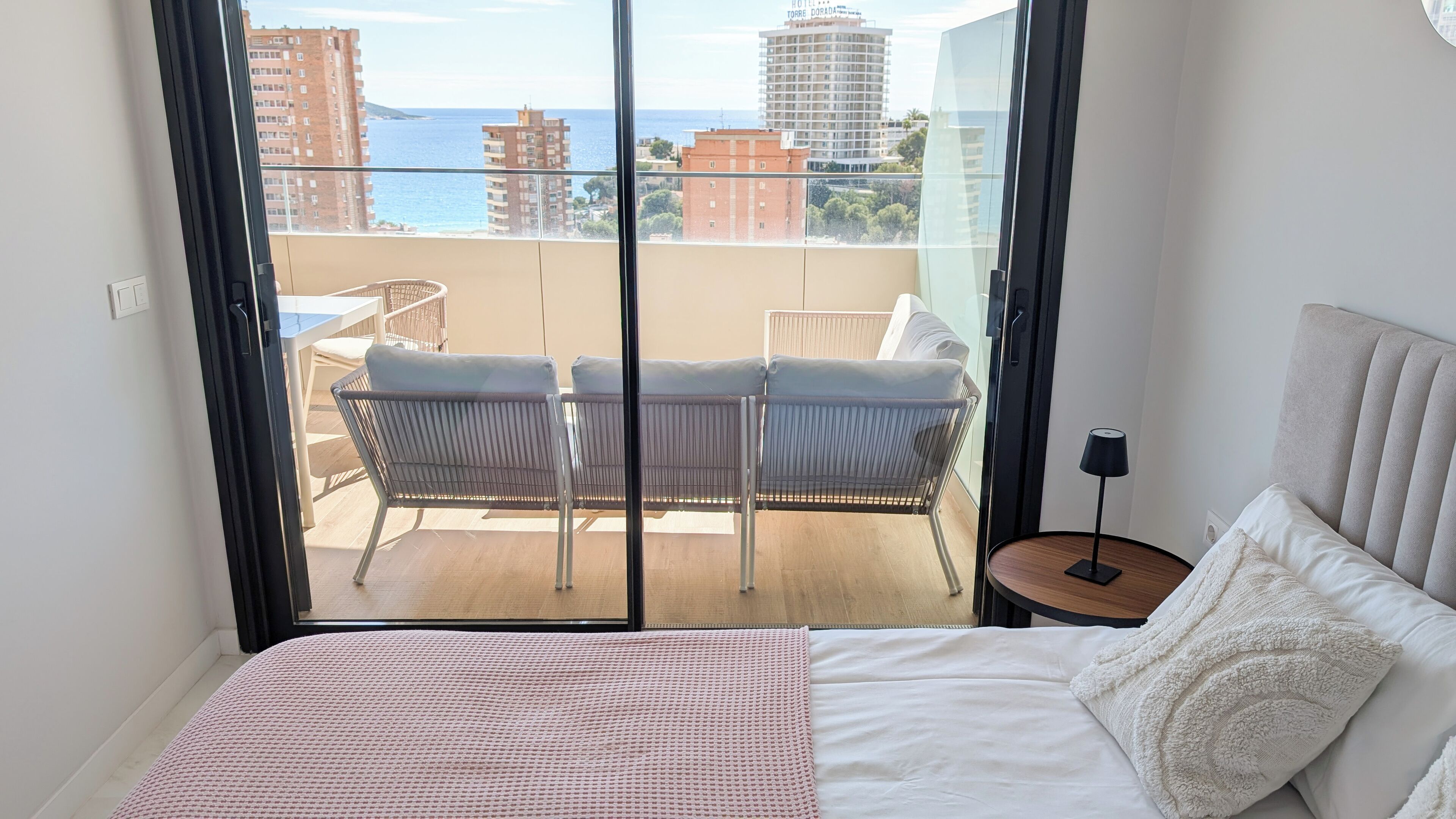 A hotel room with a balcony, a bed, a small table, and a chair.