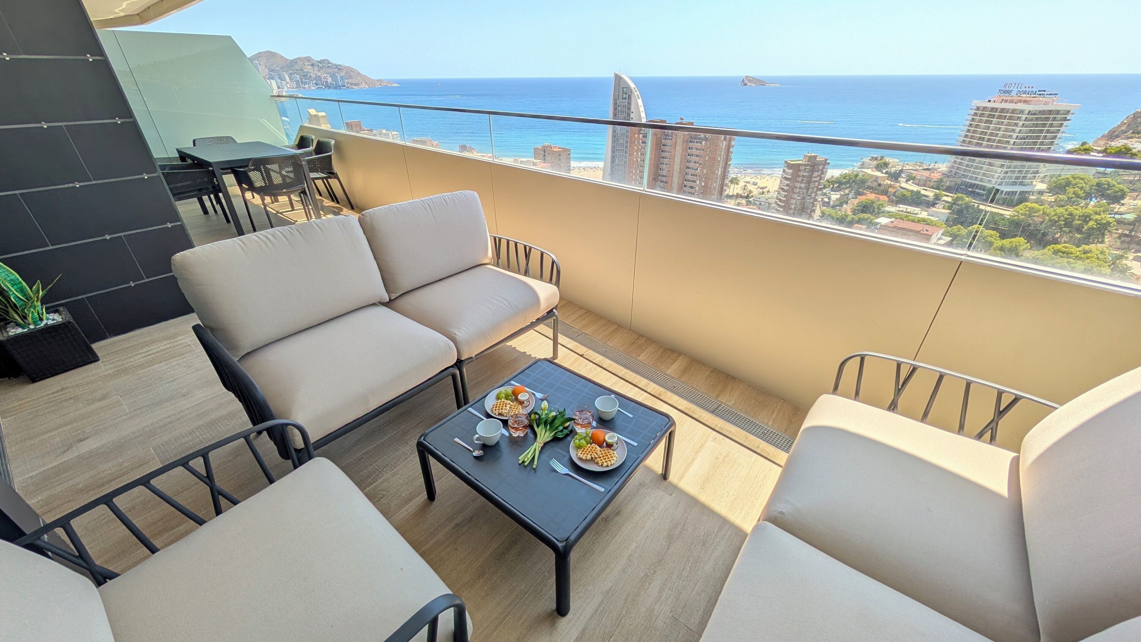 A balcony with a sofa, chairs, and a table set with waffles, fruit, and drinks.