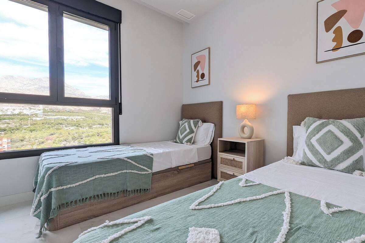 Quarto de hotel com duas camas, uma mesa de cabeceira, uma luminária e vista para uma paisagem montanhosa.