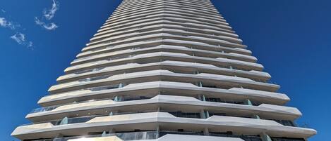 A modern high-rise building with a unique stepped design, featuring multiple balconies and large windows.