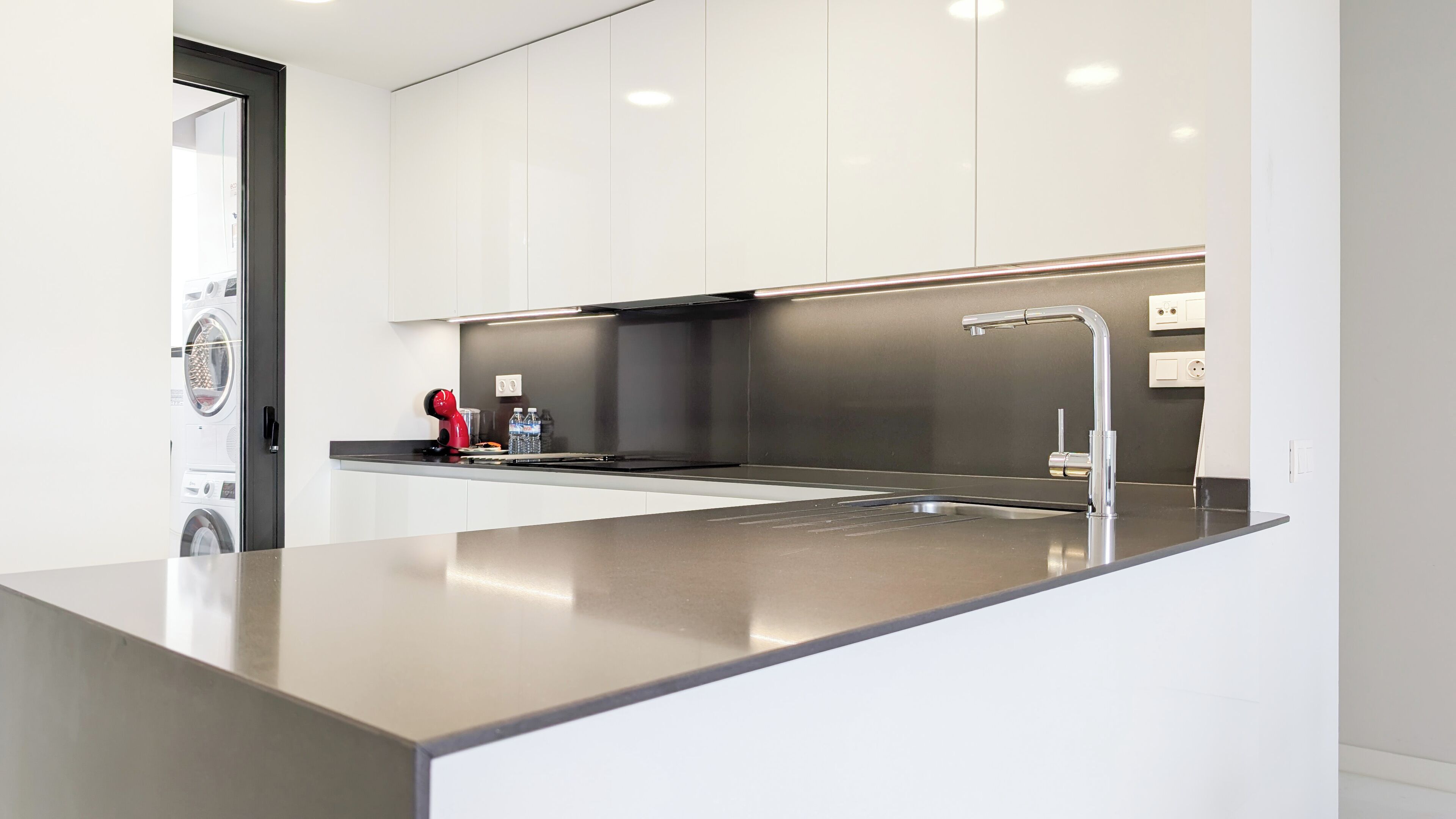 A modern kitchen with a stainless steel countertop, a built-in sink, and a red kettle.