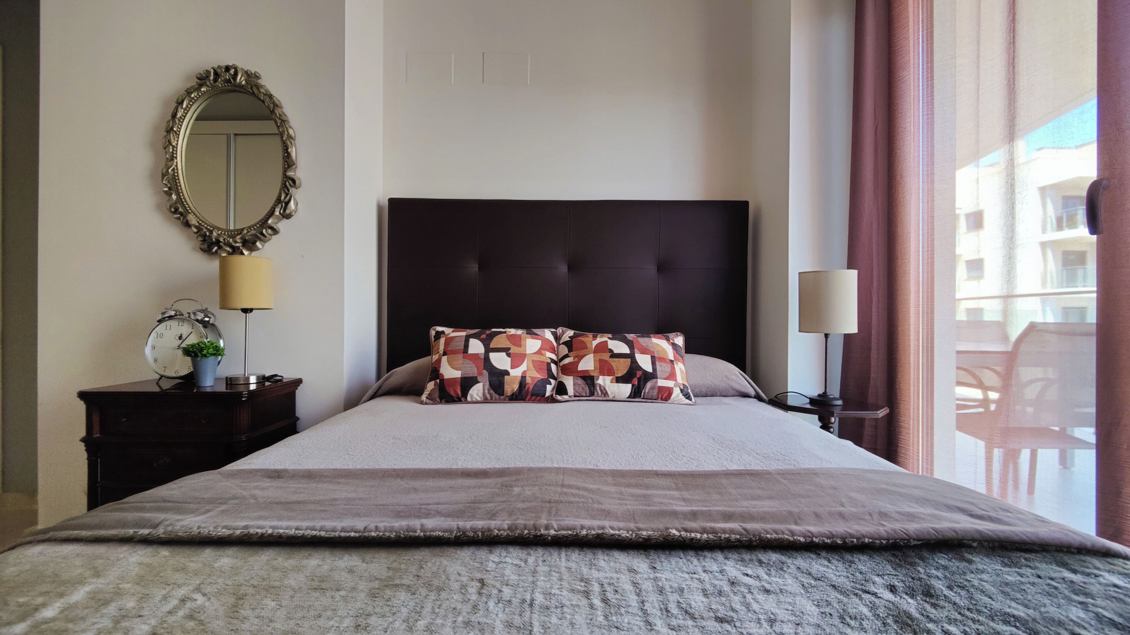 Une chambre d’hôtel avec un lit, une table de chevet, un miroir, une lampe et une vue sur l’extérieur.