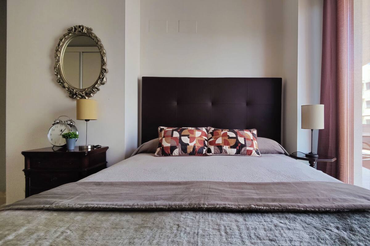 Une chambre d’hôtel avec un lit, une table de chevet, un miroir, une lampe et une vue sur l’extérieur.