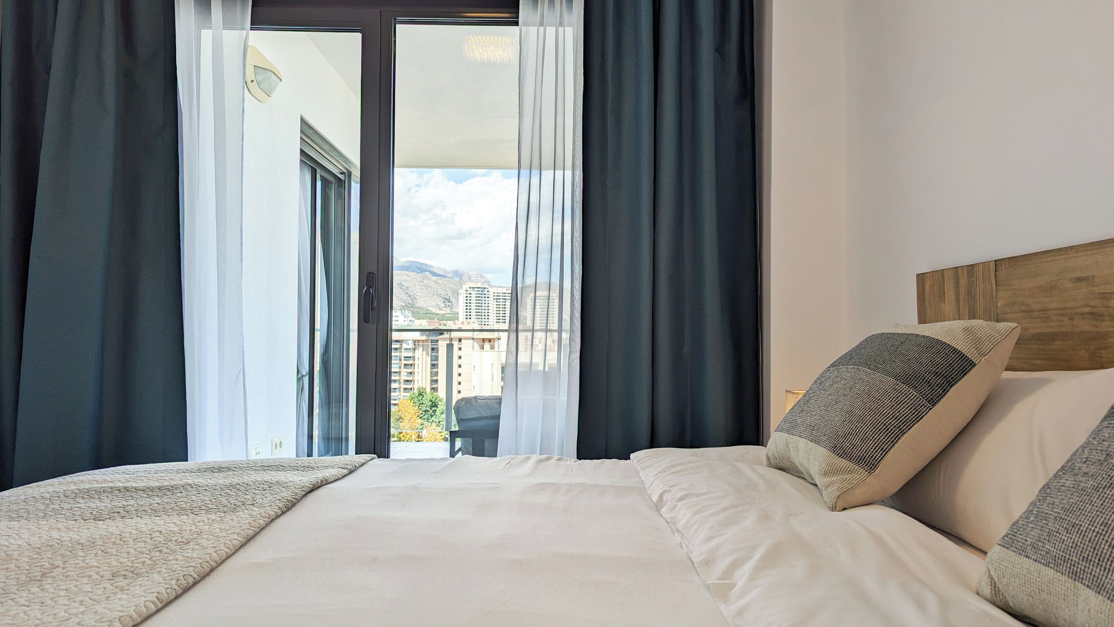 Une chambre d’hôtel avec un lit, une vue sur la ville et un balcon avec des rideaux.