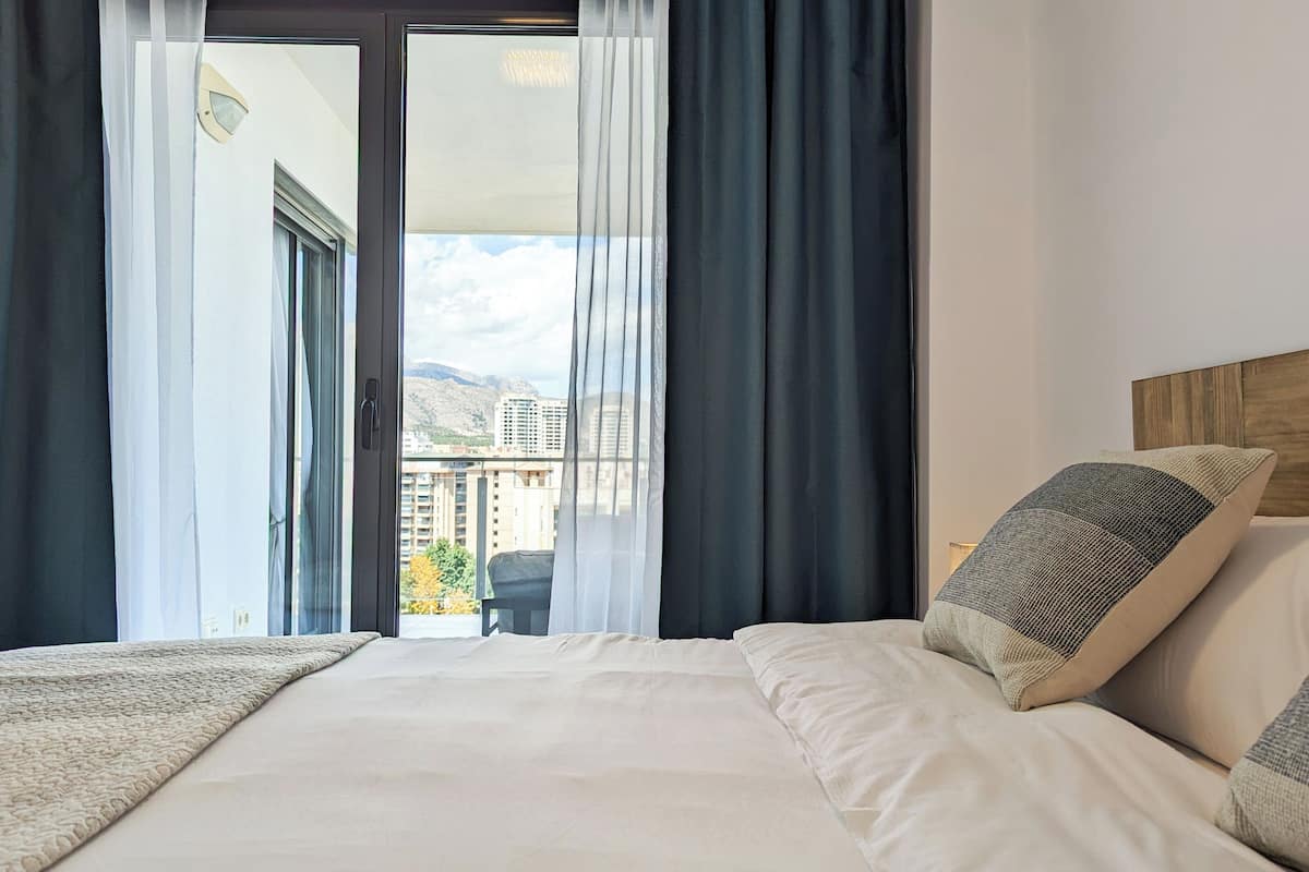 Une chambre d’hôtel avec un lit, une vue sur la ville et un balcon avec des rideaux.