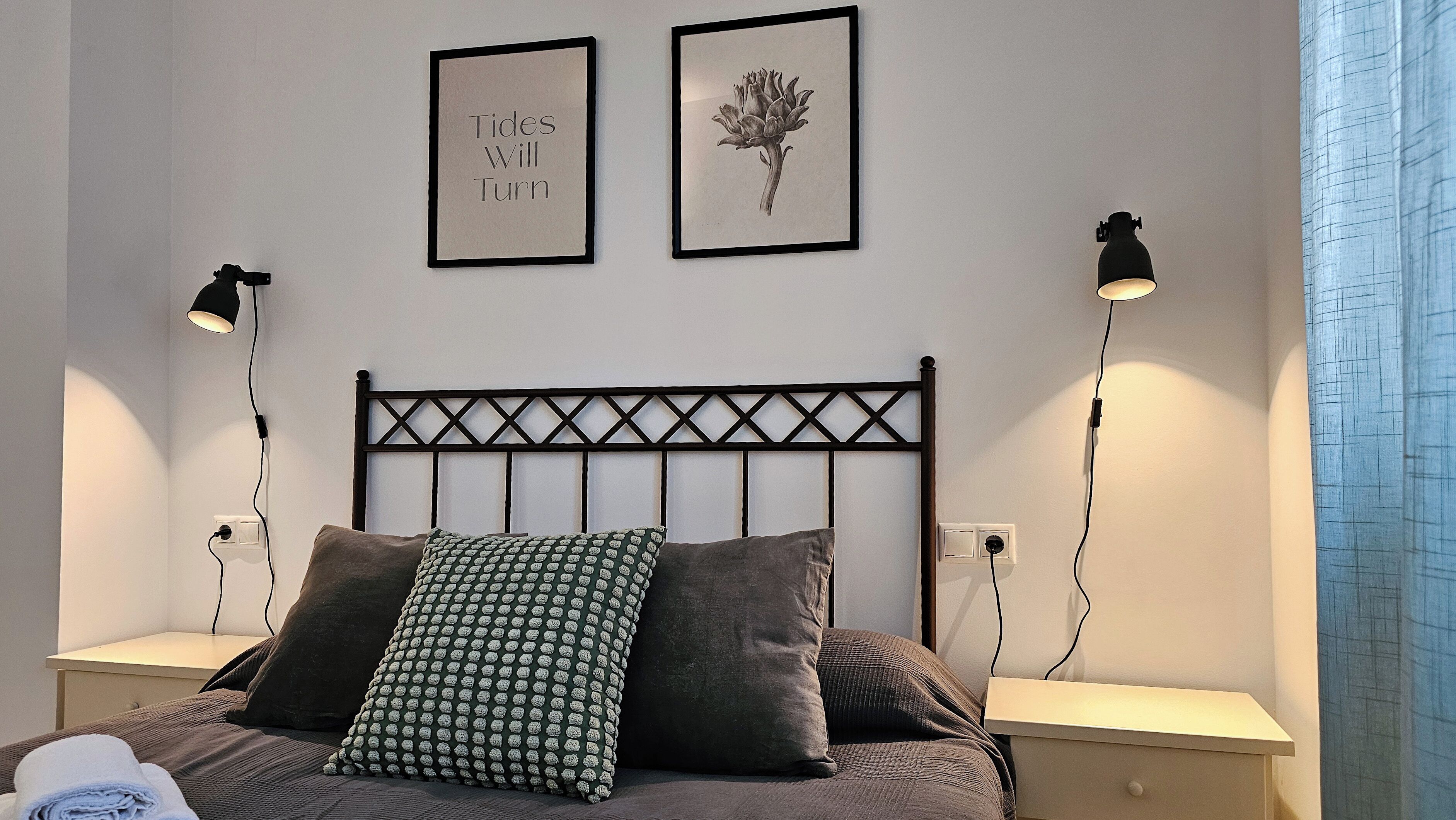 Une chambre à coucher comprenant un lit, deux tables de chevet, deux lampes fixées au mur, une tête de lit et deux tableaux encadrés.