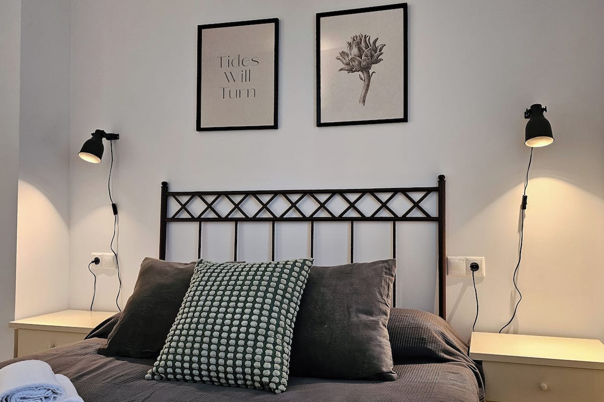 Une chambre à coucher comprenant un lit, deux tables de chevet, deux lampes fixées au mur, une tête de lit et deux tableaux encadrés.