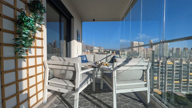 Uma varanda com sofá, cadeiras, uma mesa e vista para a cidade.