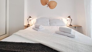 Quarto de hotel com cama, duas luminárias de cabeceira, luminária na parede e janela com cortinas.