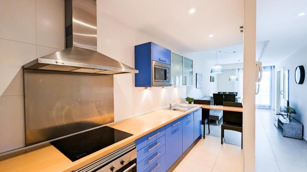 A modern kitchen with a stainless steel range hood, a microwave, and blue cabinets.