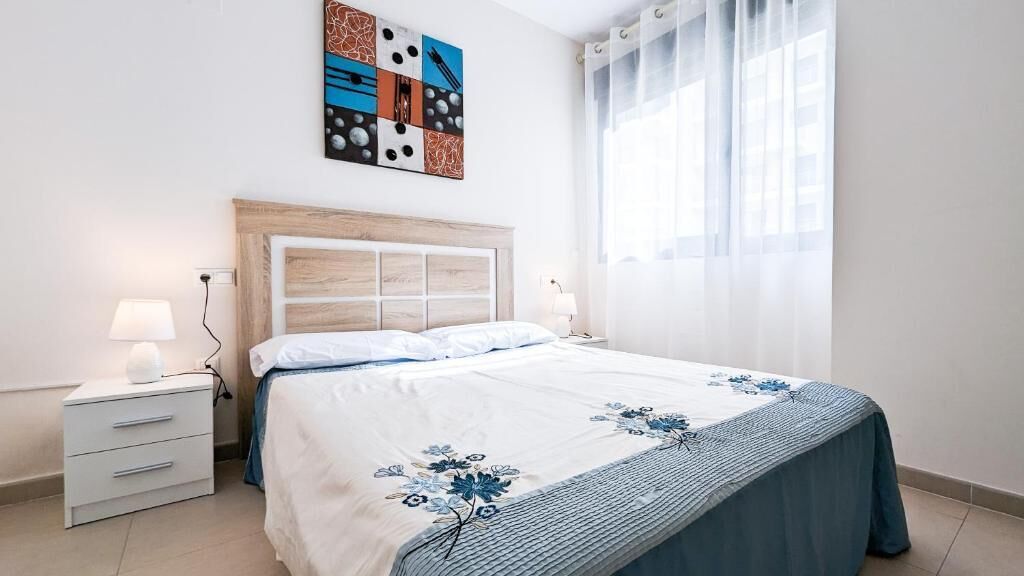 A bedroom with a bed, bedside tables, a wall art piece, and a window with curtains.