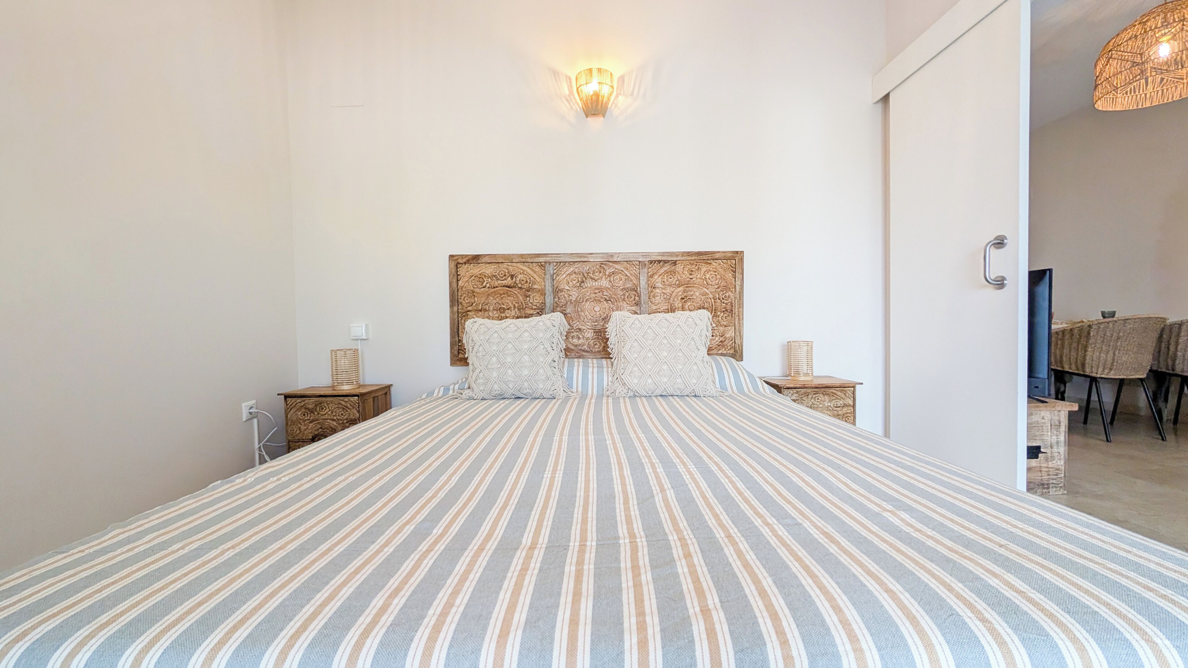 Une chambre à coucher avec un grand lit, une tête de lit en bois, deux tables de chevet et un luminaire fixé au mur.