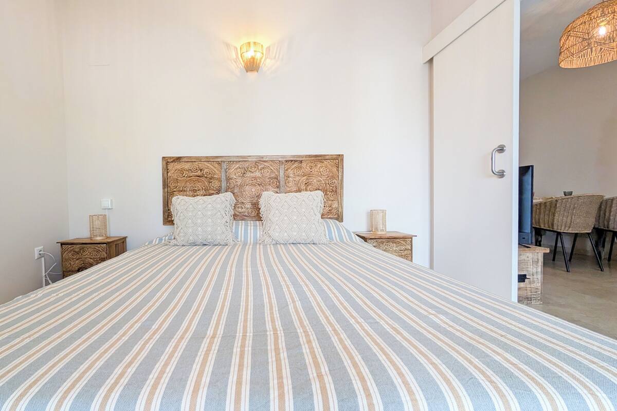 Une chambre à coucher avec un grand lit, une tête de lit en bois, deux tables de chevet et un luminaire fixé au mur.