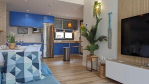 Uma sala de estar moderna com um sofá, uma televisão e uma cozinha ao fundo.