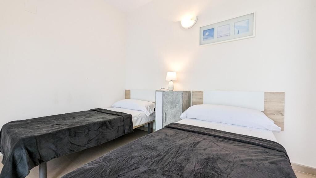 A room with two beds, a nightstand with a lamp, and a framed picture on the wall.