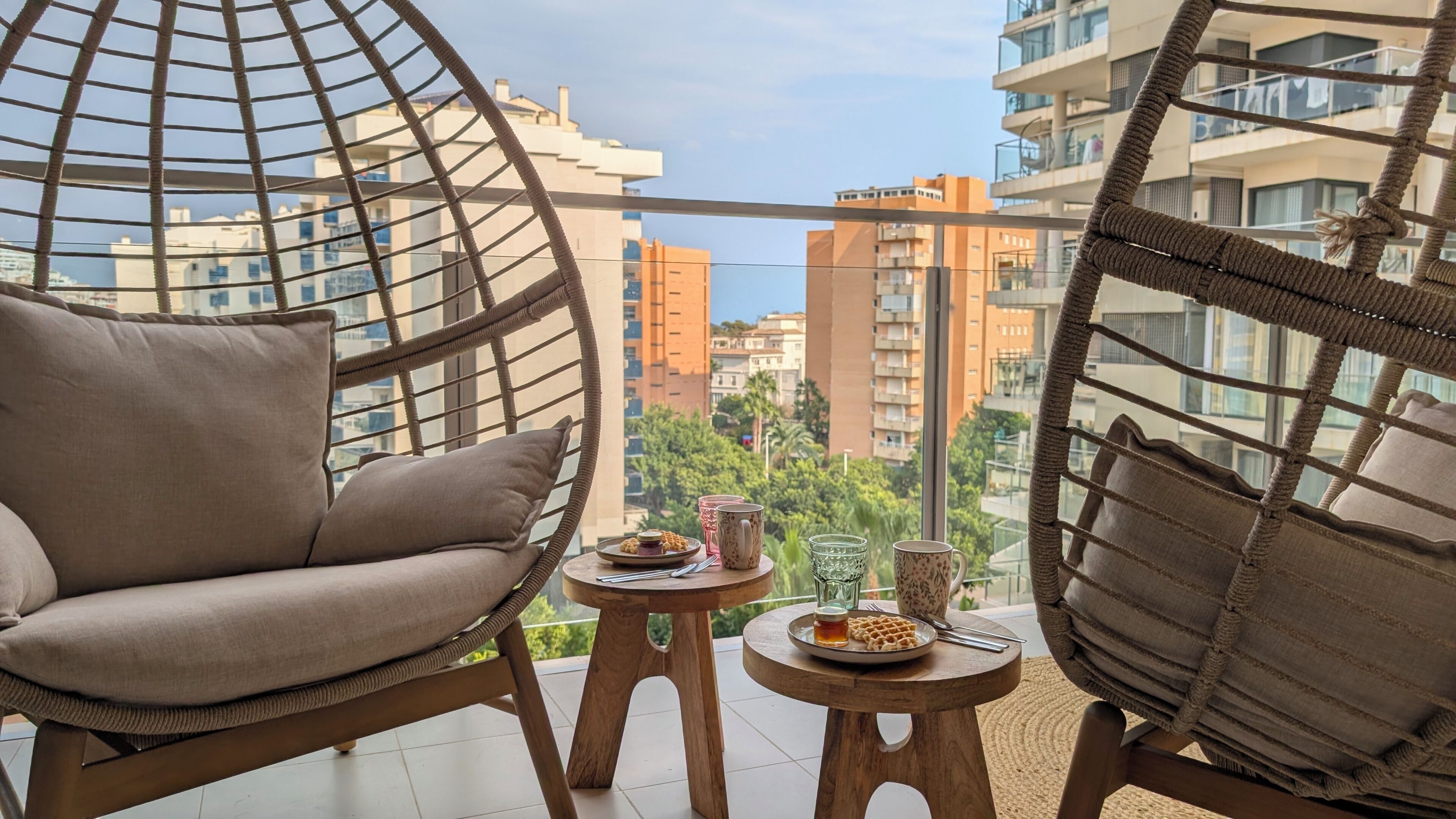 Ein Balkon mit zwei Korbstühlen, einem kleinen Tisch mit einer Speiseplatte, einem Glas und einer Tasse.