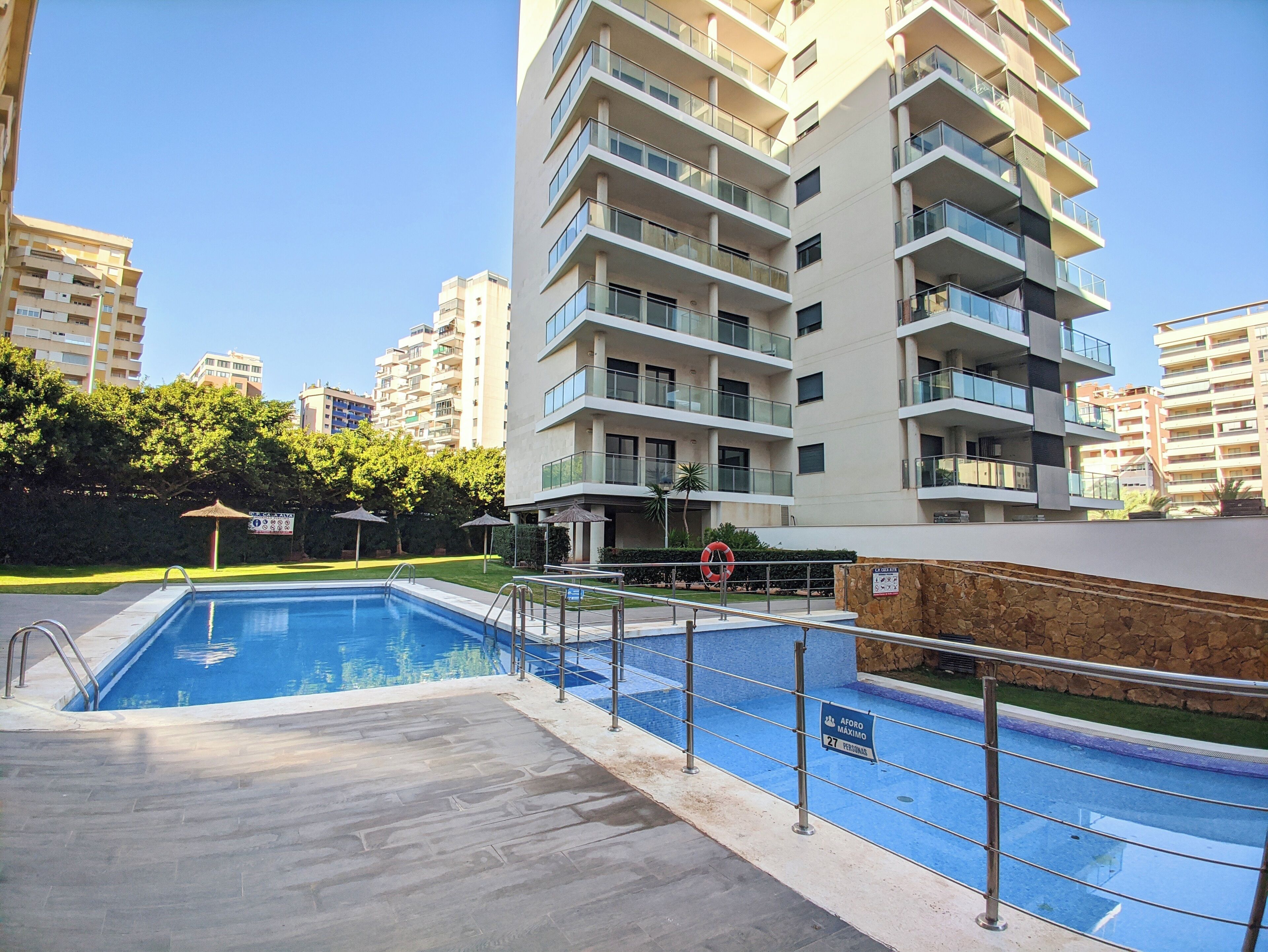 A residential building with a swimming pool, multiple balconies, and a clear sky.