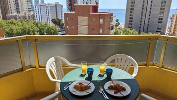 Un balcón con una mesa dispuesta para el desayuno, dos platos con cruasanes, dos vasos de zumo de naranja y una taza azul.