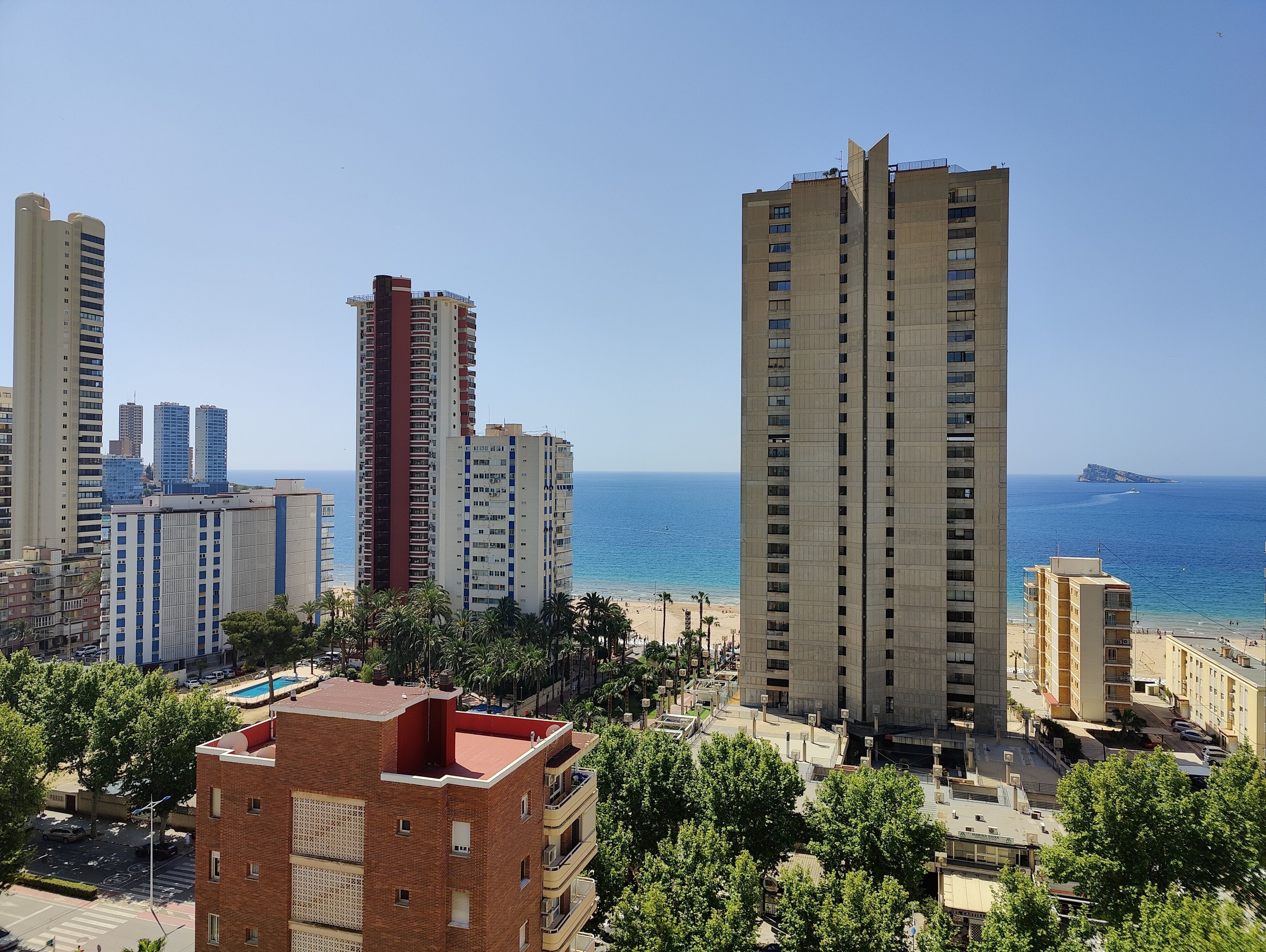 Paisatge urbà costaner amb edificis alts, una platja i cel blau.