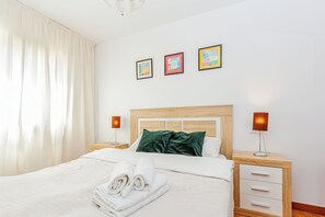 Un letto rifatto con cuscini, una lampada da comodino e un tavolino notte con una lampada. Tre quadri appesi alla parete.