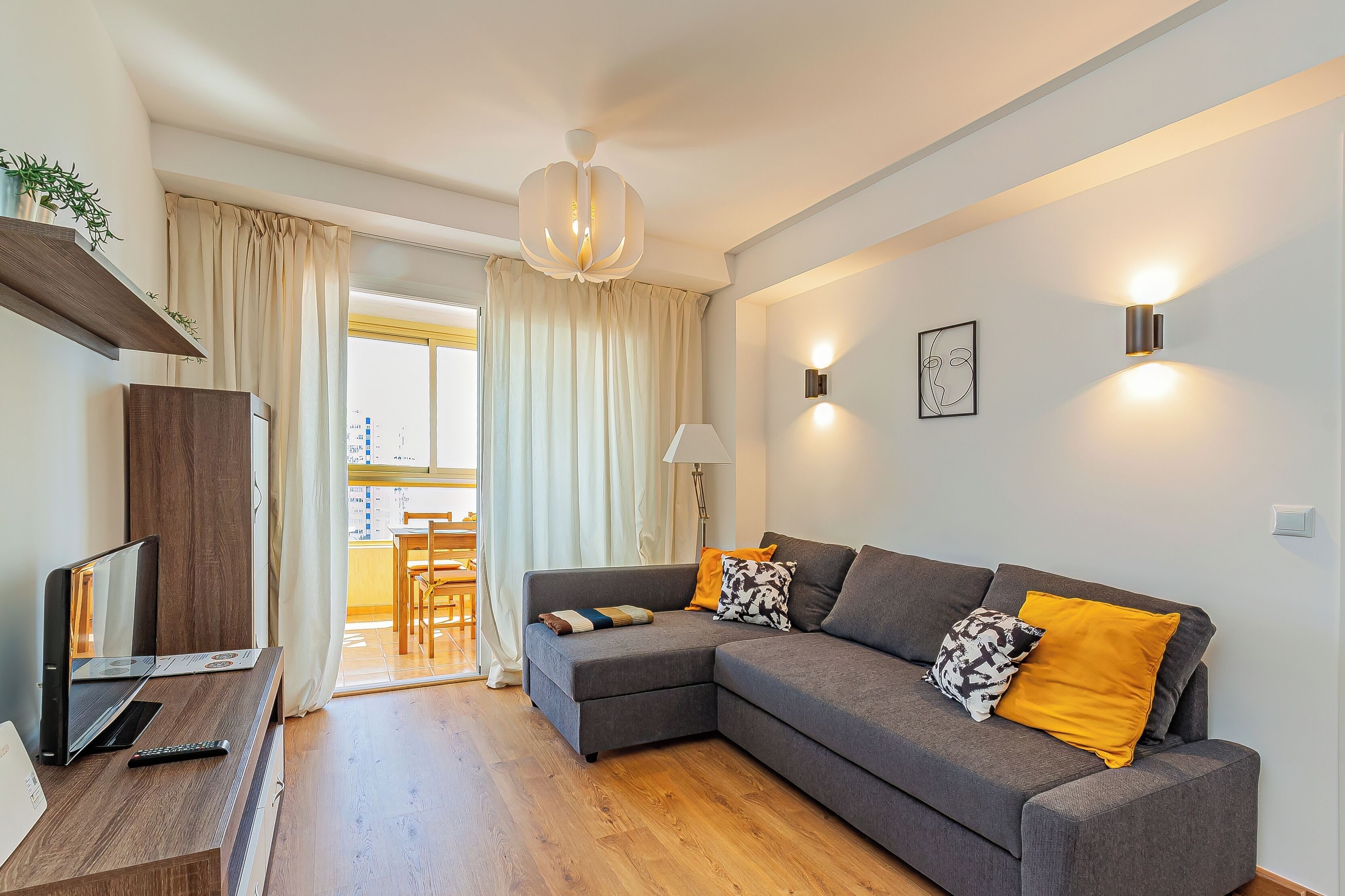 A modern living room with a grey sectional sofa, a wooden TV stand, and a ceiling light fixture.