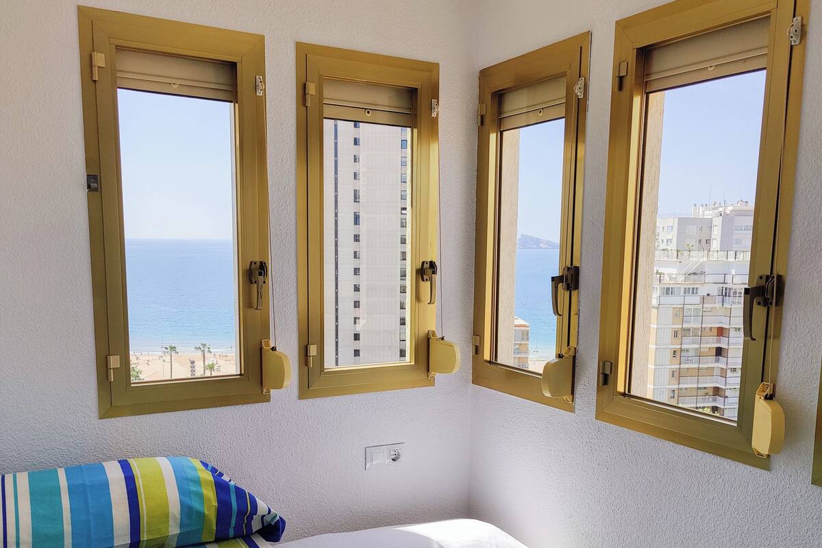 A room with a bed, two windows, and a view of the sea.
