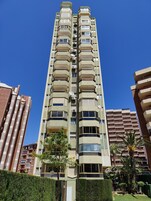 Un edificio alto con varios balcones, cielo despejado y vegetación circundante.