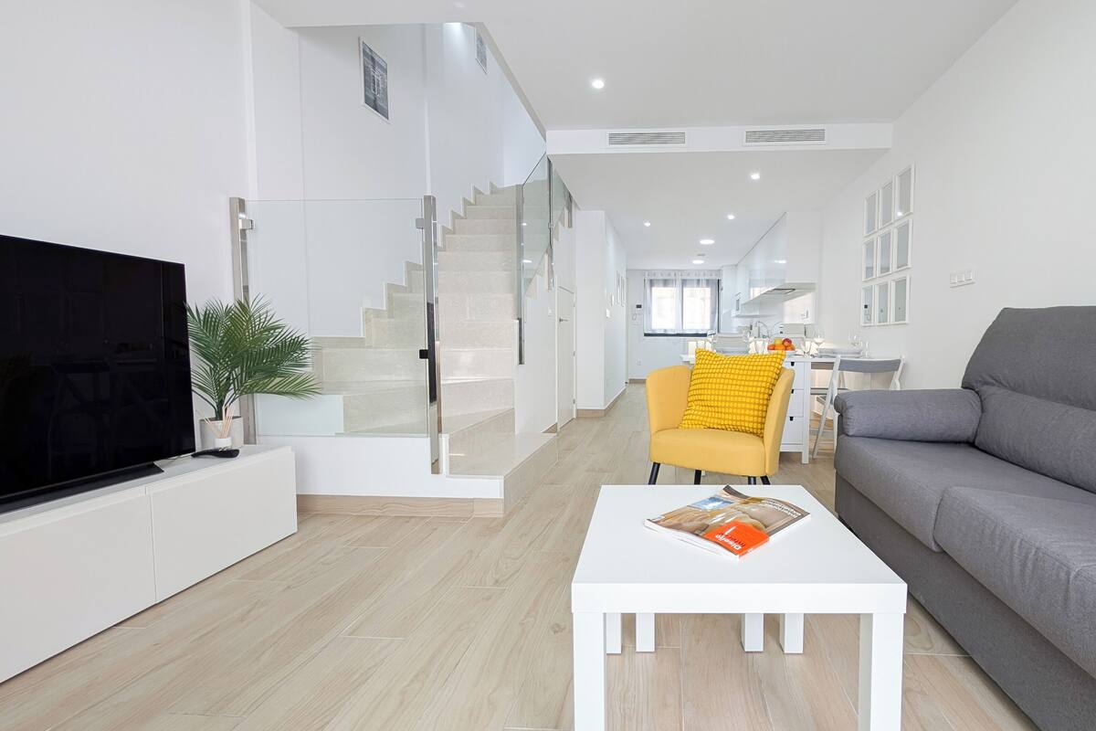 A modern living room with a flat-screen TV, a sofa, a coffee table, and a staircase leading to an upper floor.