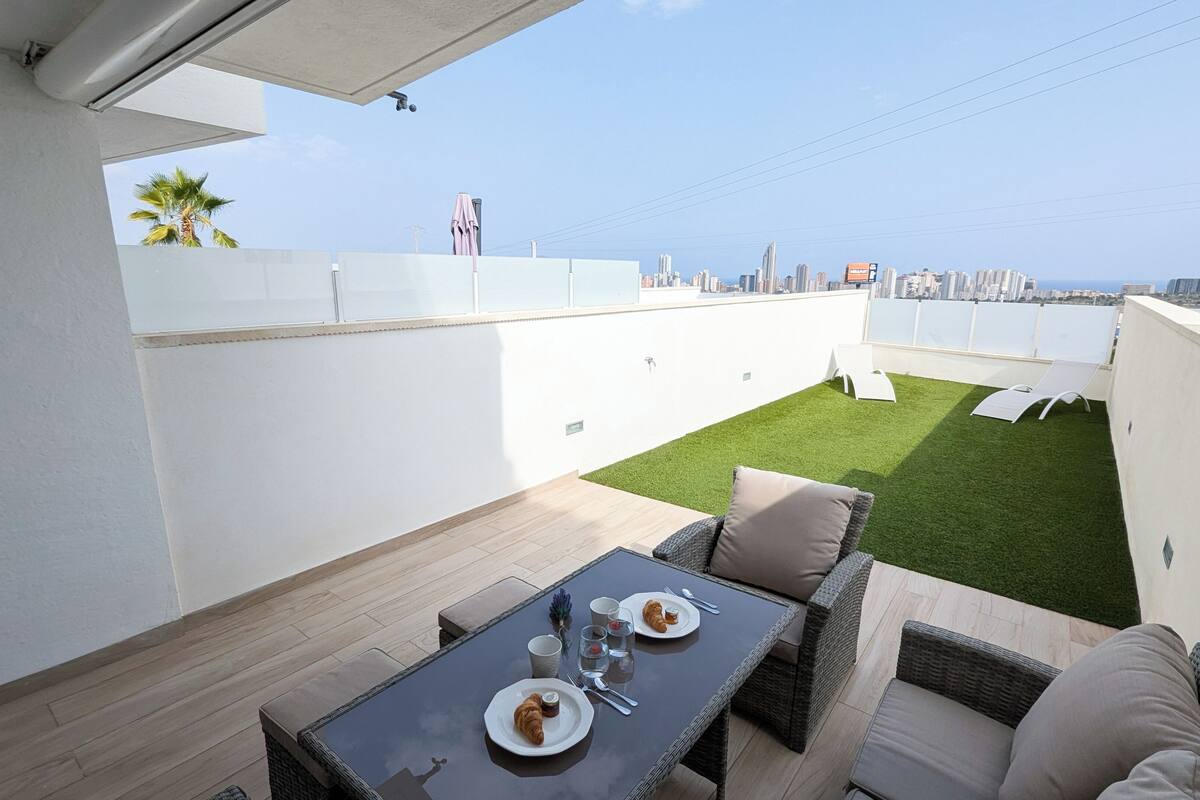 A rooftop terrace with a dining table, chairs, and a small lawn area.