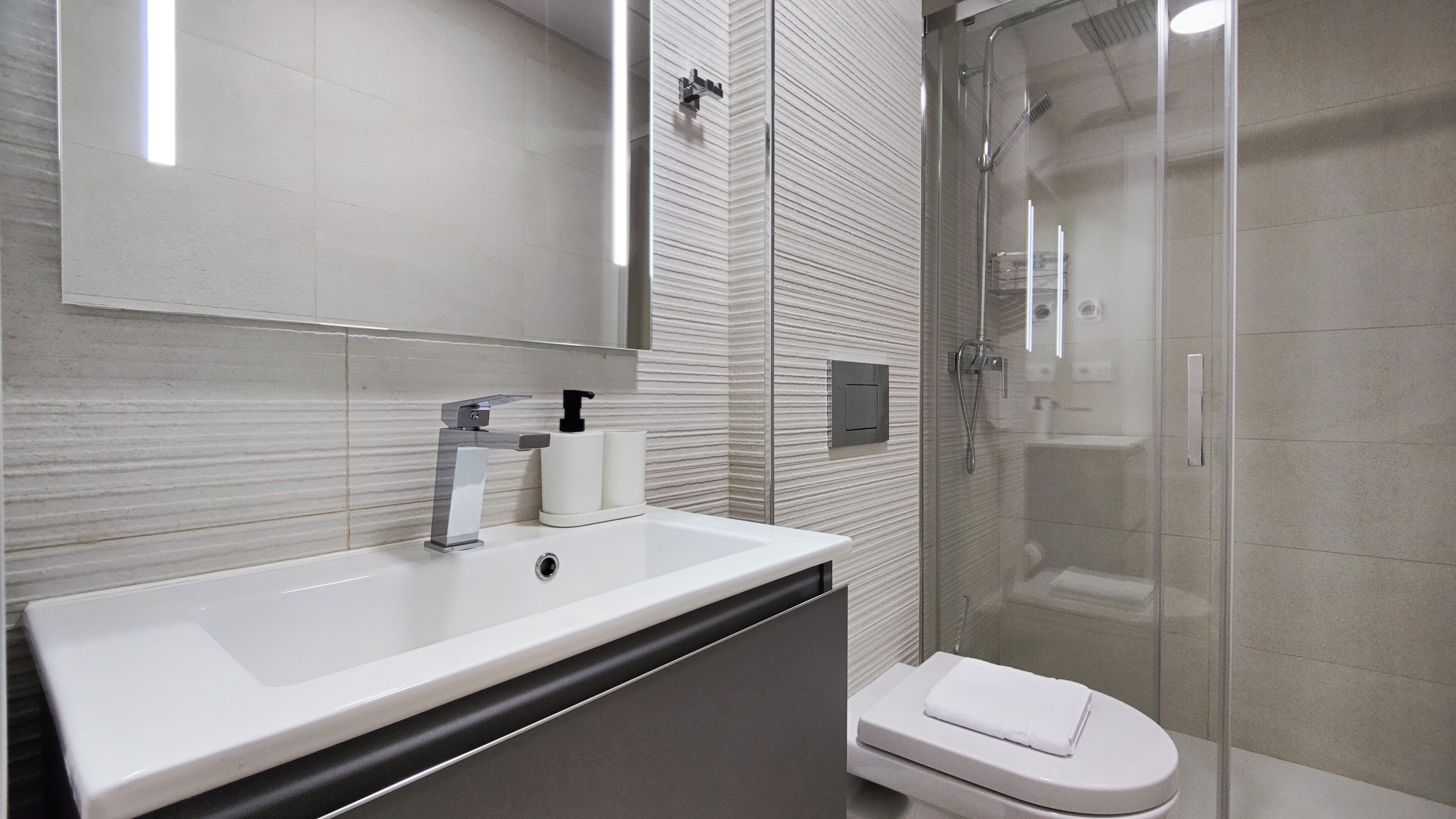 A modern bathroom with a white sink, a glass shower enclosure, and a toilet.