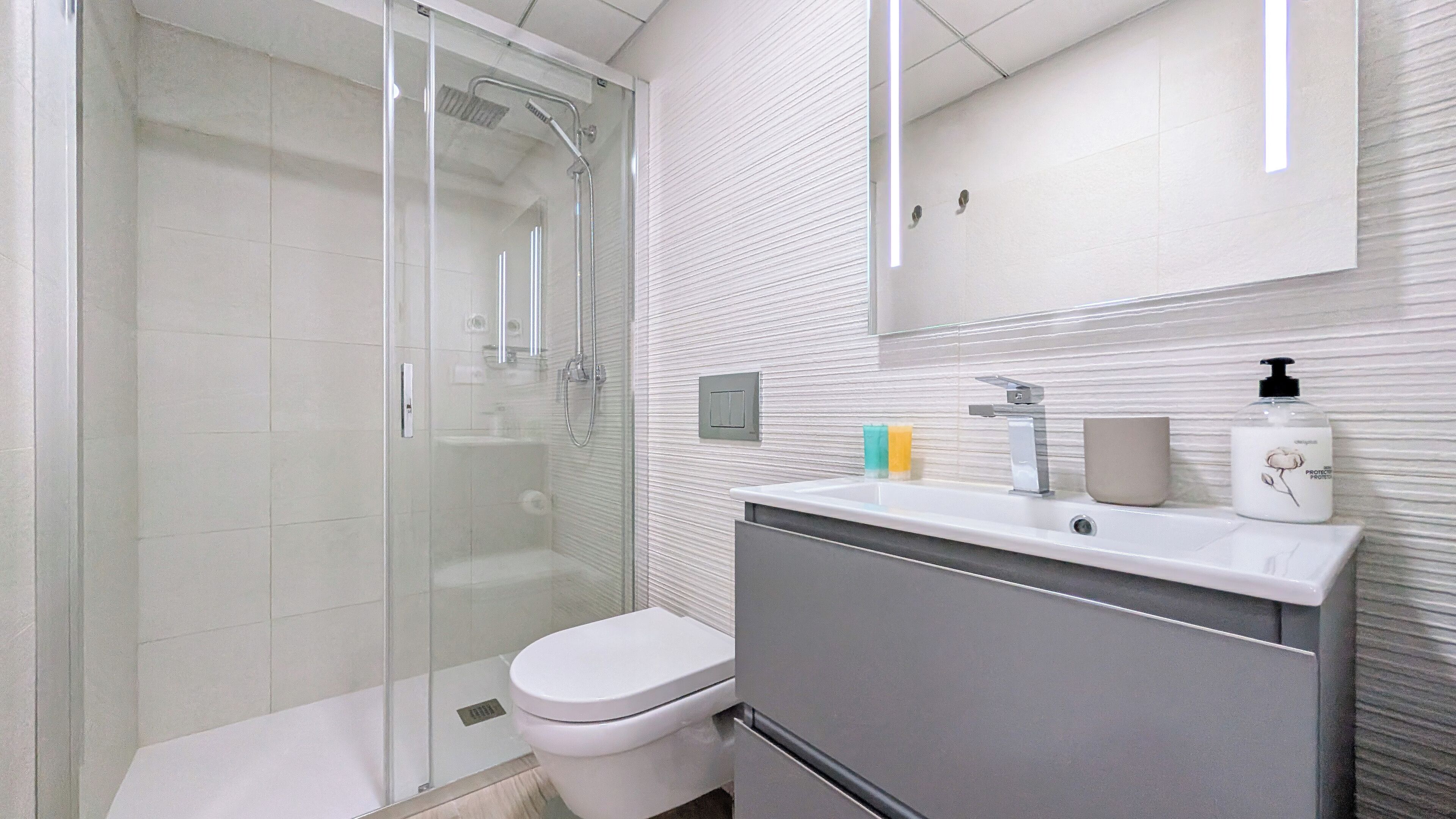A modern bathroom with a glass shower enclosure, a toilet, a sink with a mirror above, and toiletries on the sink.