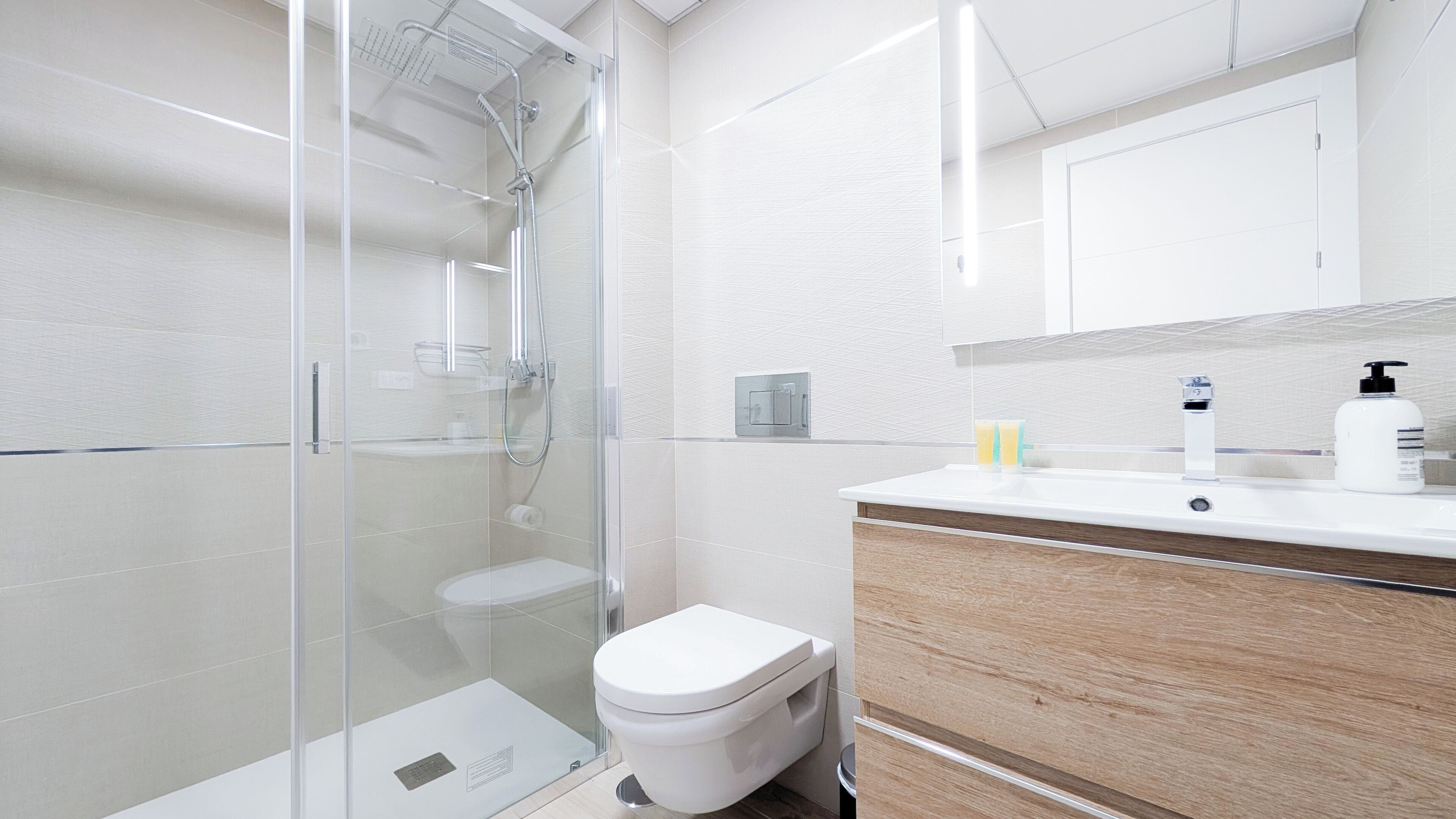 Une salle de bain moderne avec une douche à parois de verre, des toilettes blanches et un meuble-lavabo en bois avec un miroir.