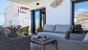 A modern outdoor seating area with wicker furniture, a sofa, and a table set for breakfast. - Panoramic Apartments (Finestrat)