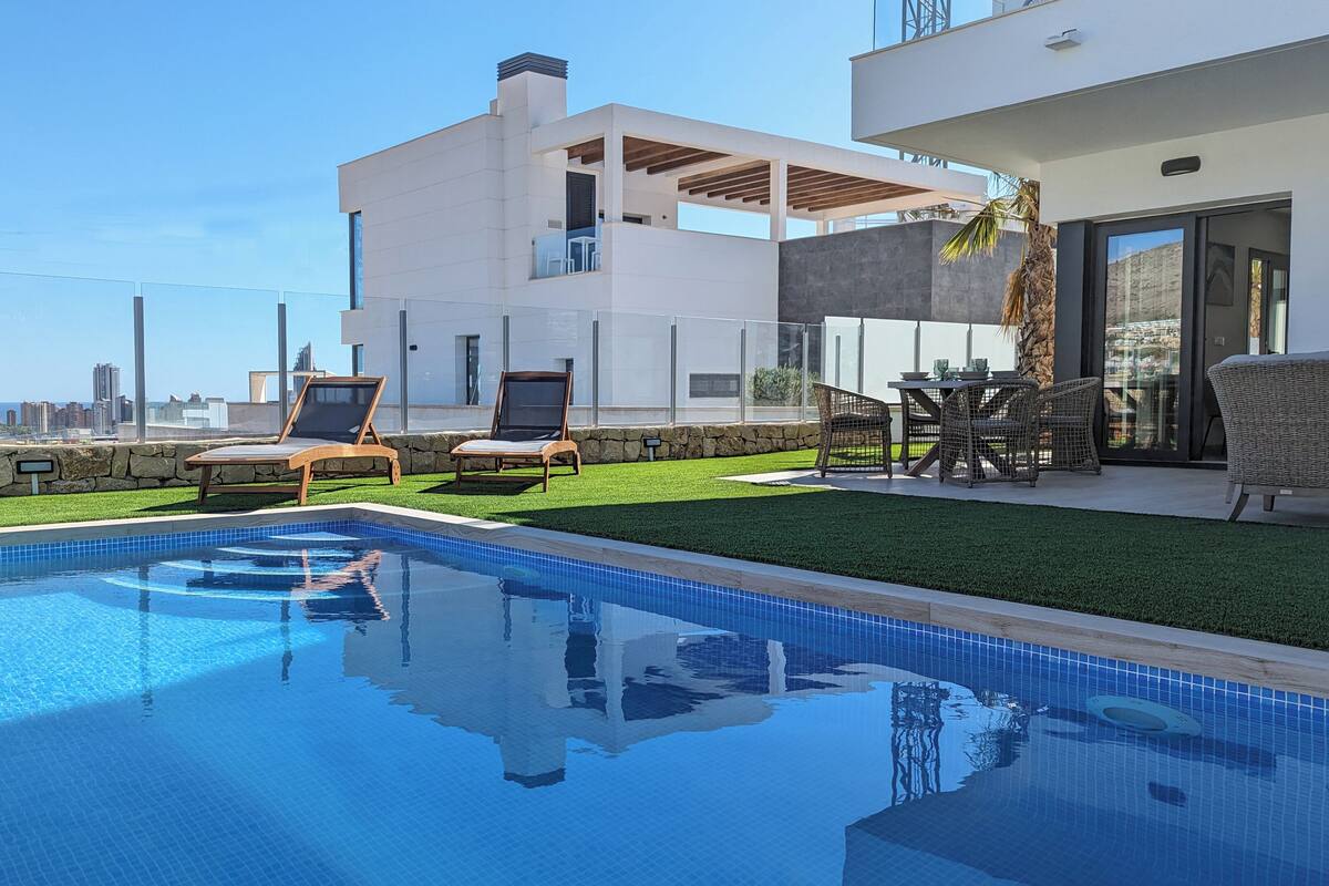 A modern pool area with two lounge chairs, a dining table with chairs, and a stone wall.