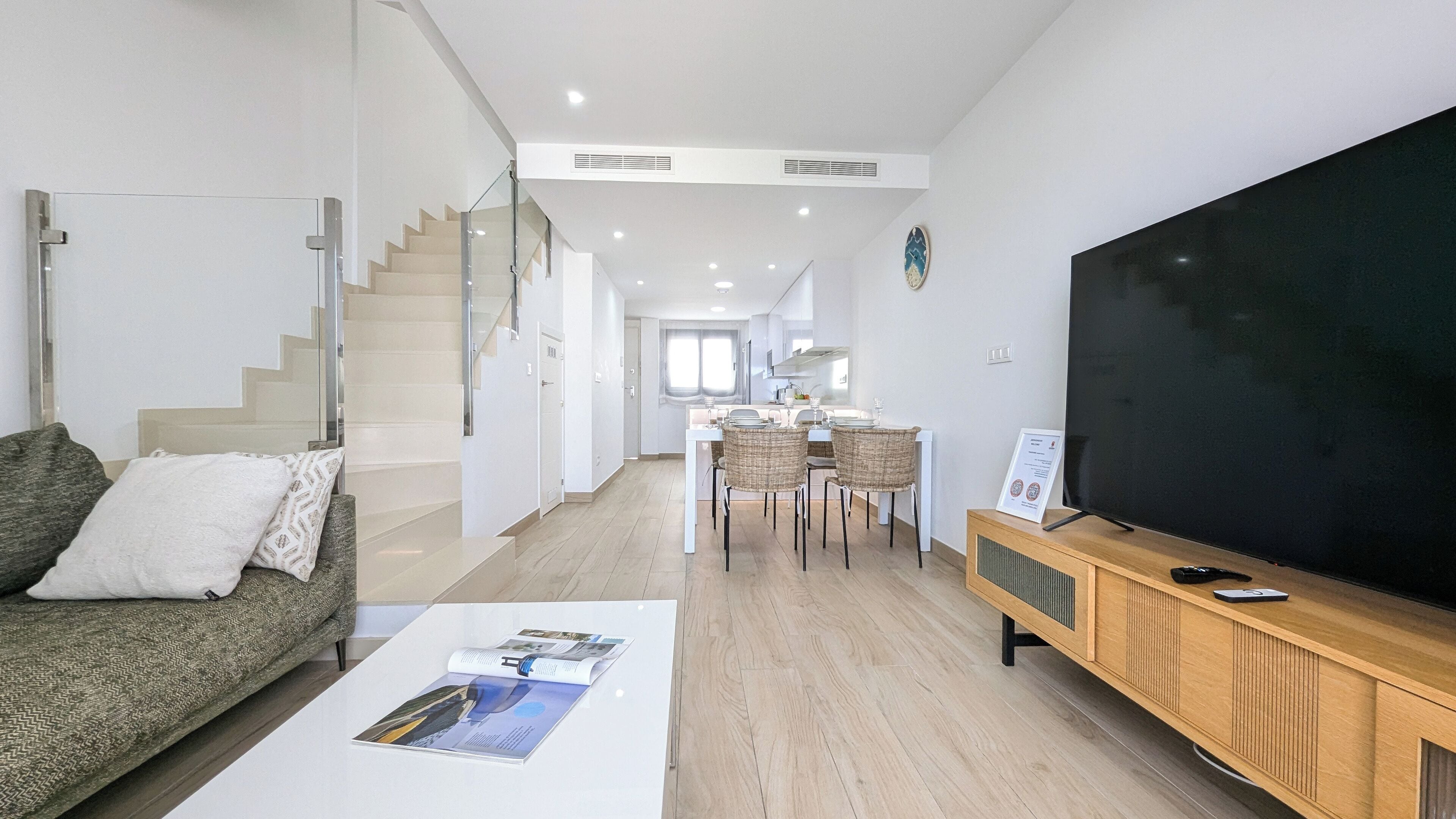 A modern living room with a sofa, coffee table, TV, and a dining area with chairs and a table.