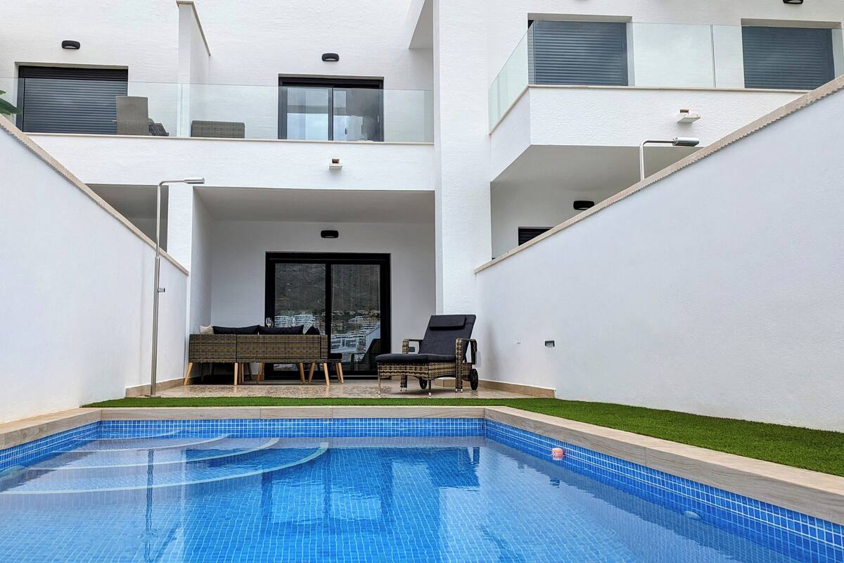 A modern residential building with a swimming pool, outdoor seating, and a view of the surrounding area.