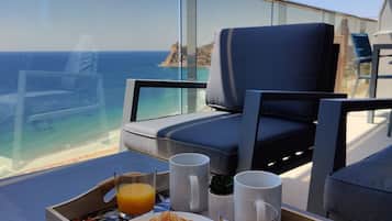 Bandeja de desayuno con cruasanes y jugo de naranja en un balcón con vista al océano.