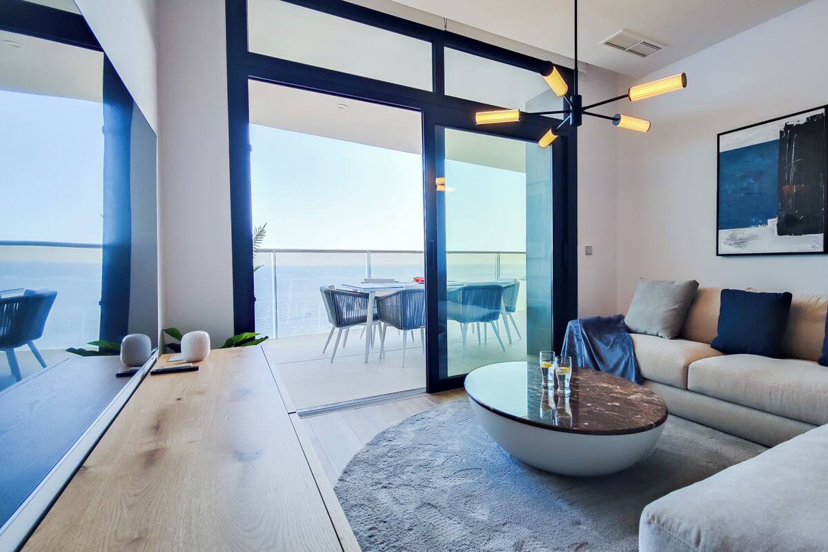 Uma sala de estar moderna com um sofá, uma mesa de centro e uma varanda com vista para o mar.