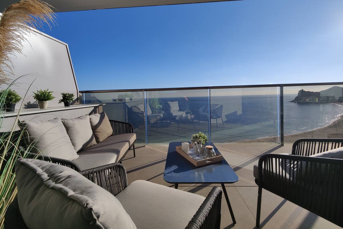 Uma varanda com vista para o mar, equipada com sofá, cadeiras e uma mesa.