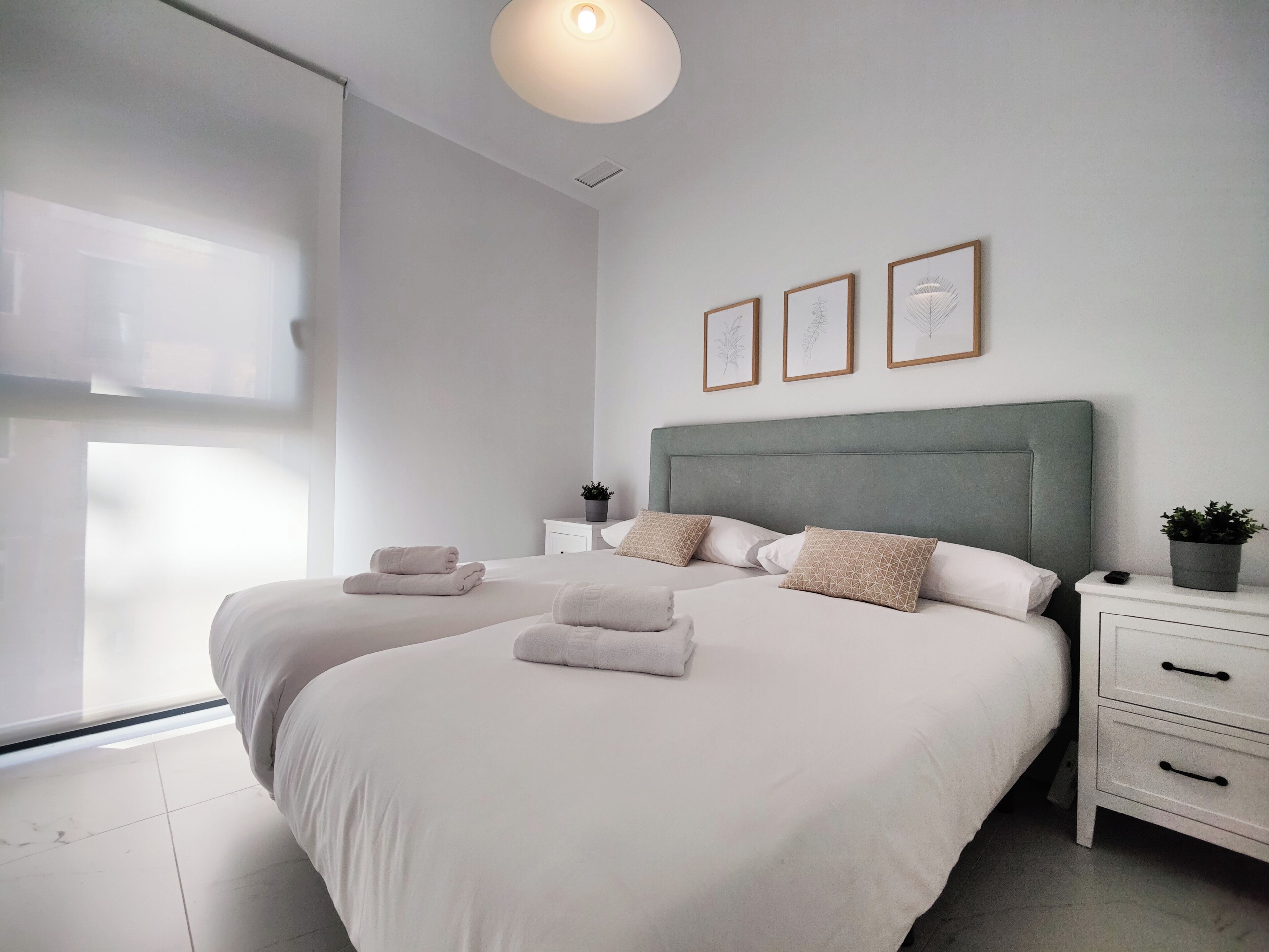Ein modernes Schlafzimmer mit zwei Betten, einem großen Fenster und einer Deckenleuchte.