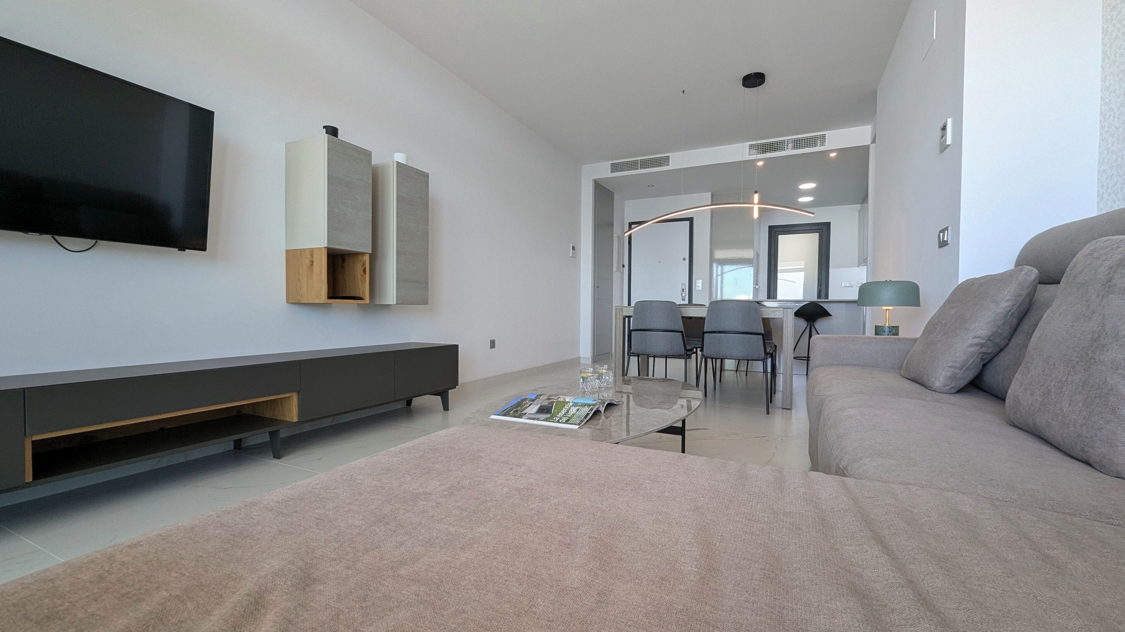 A modern living room with a flat-screen TV, a sofa, a coffee table, and a dining area with chairs.
