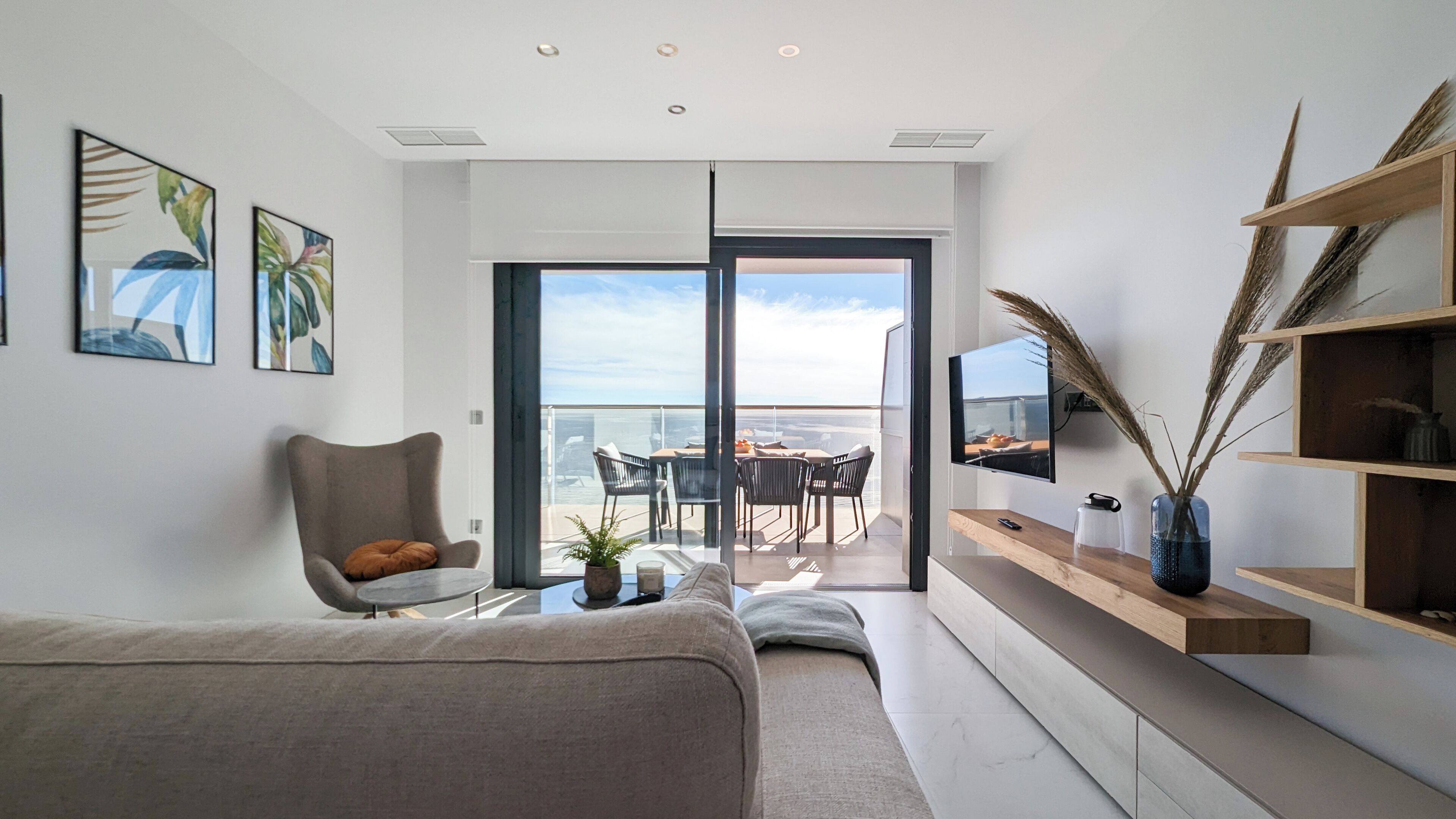 A modern living room with a sofa, a dining table, chairs, a TV, and a balcony with a view.