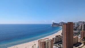 A coastal cityscape with a beach, high-rise buildings, and a distant fort. - Sunset Cliffs Apartments Tower 2 (Benidorm)