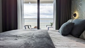 A bedroom with a large bed, a view of the sea, and a potted plant. - Sunset Cliffs Apartments Tower 2 (Benidorm)
