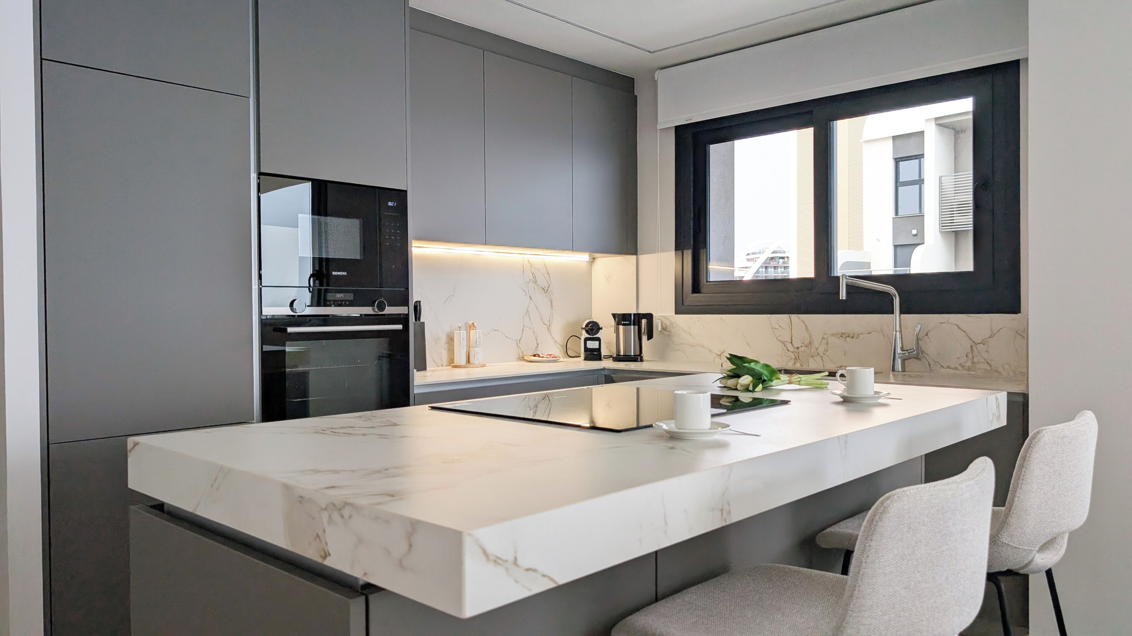 A modern kitchen with a built-in oven, a coffee maker, and a window above the sink.