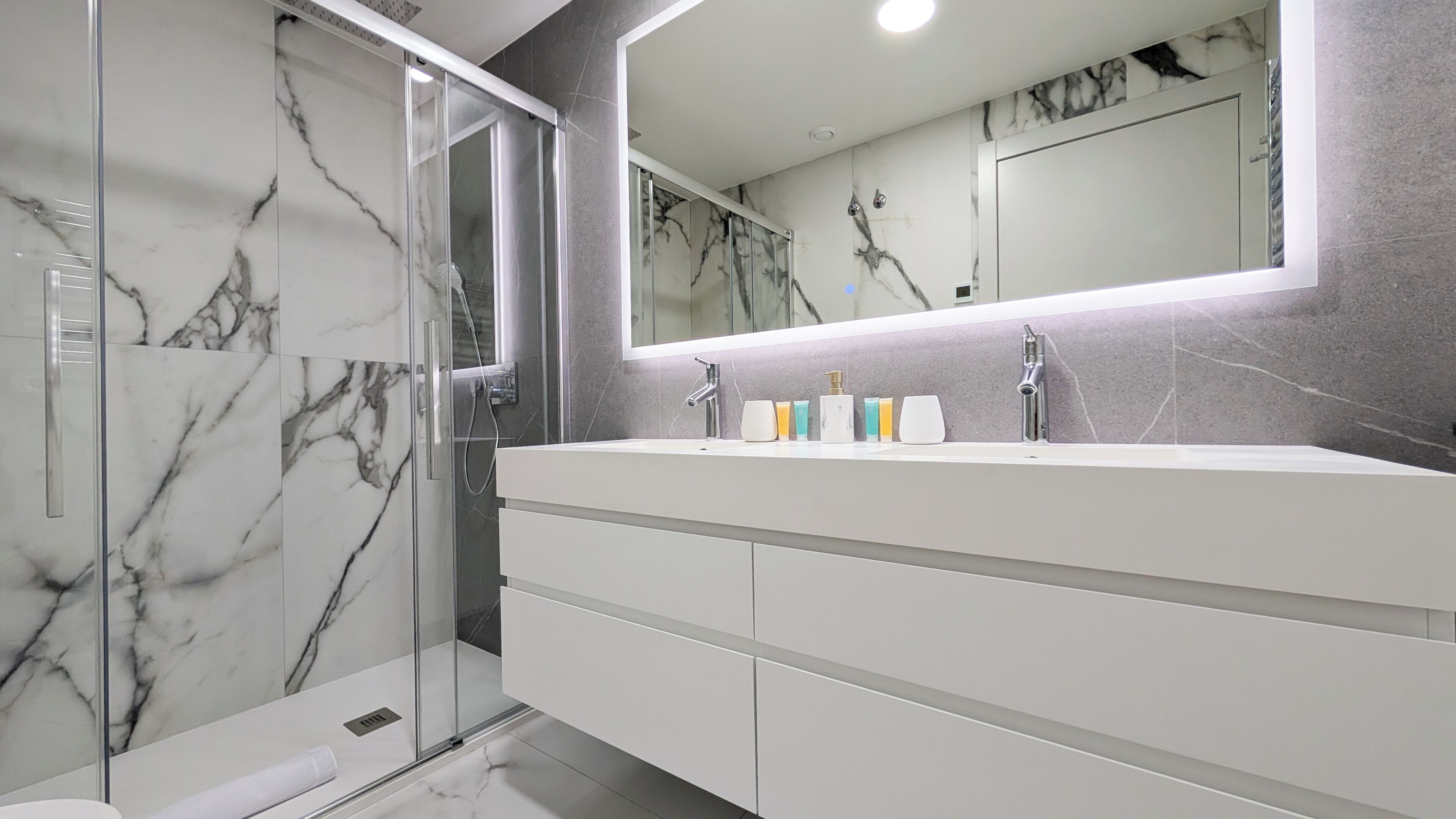 A modern bathroom with a glass shower enclosure, a large mirror, and a white vanity with multiple storage drawers.