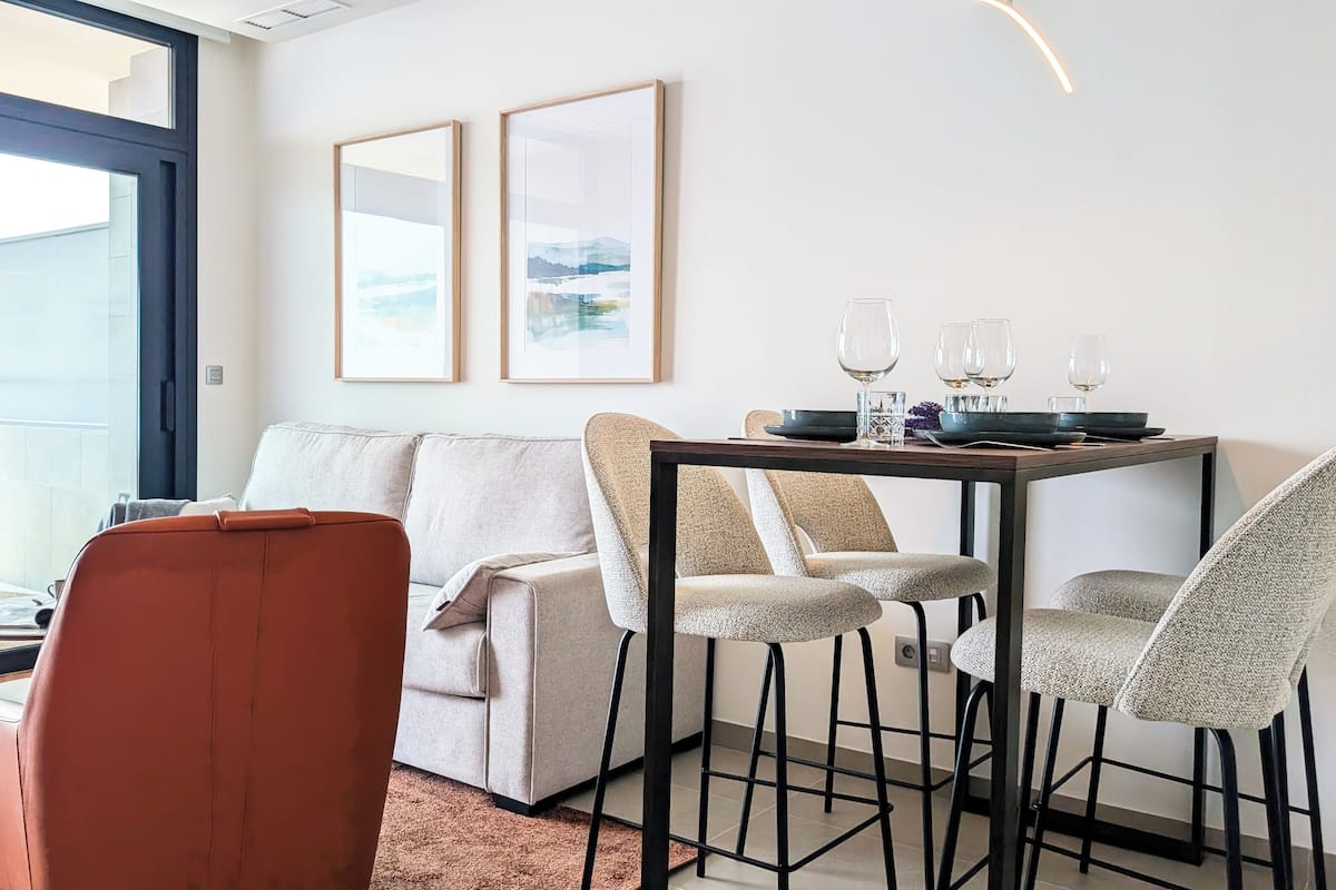 En moderne stue med sofa, to stole, et spisebord med glas og indrammet kunst på væggen.